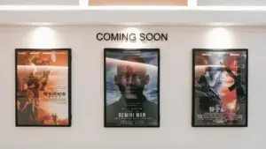 Kino teatro sienoje iškabinti būsimų filmų plakatai su apšvietimu laukiamajame.
