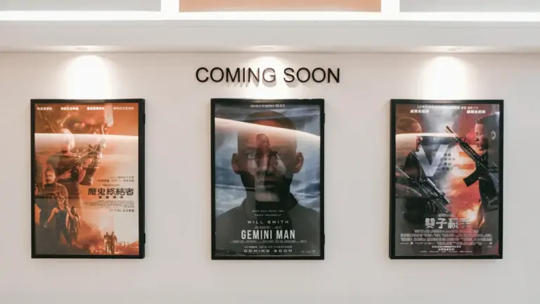 Kino teatro sienoje iškabinti būsimų filmų plakatai su apšvietimu laukiamajame.