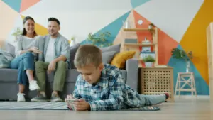 Berniukas žaidžia telefonu svetainėje, o tėvai stebi jį nuo sofos