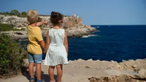 Du vaikai stovi prie jūros ir žvelgia į tolį, svajodami apie keliones.