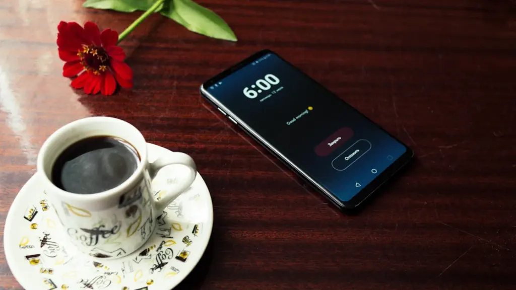 Išmanusis telefonas ir puodelis kavos ant stalo ryto metu