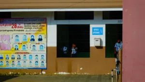 Mokiniai prie mokyklos pastato informacinio stendo su pasiekimų rezultatais.