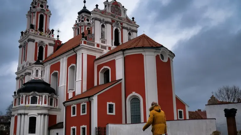 Žmogus su geltona striuke eina pro istorinę raudonos ir baltos spalvos Vilniaus bažnyčią.