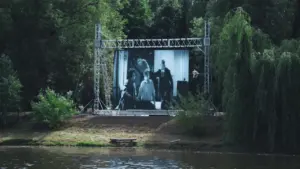 Didelis lauko kino ekranas pastatytas parke prie upės kranto vasaros metu.
