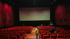 Tuščia kino salė su raudonomis kėdėmis ir dideliu ekranu pasiruošusi kino seansui.