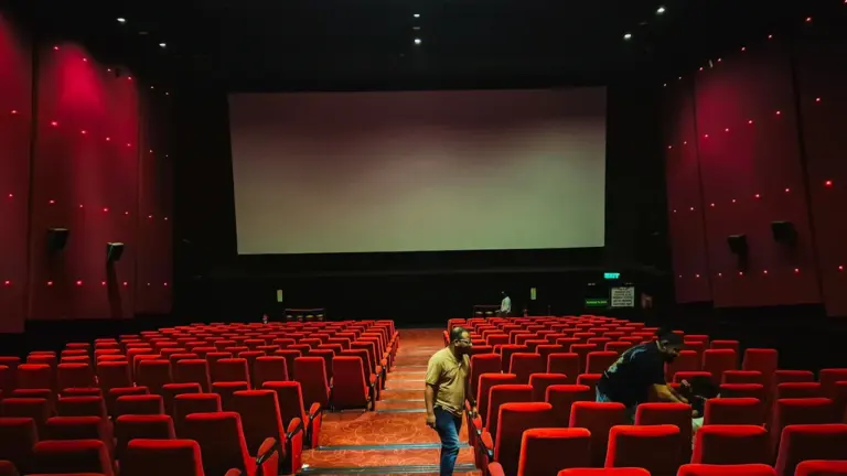 Tuščia kino salė su raudonomis kėdėmis ir dideliu ekranu pasiruošusi kino seansui.