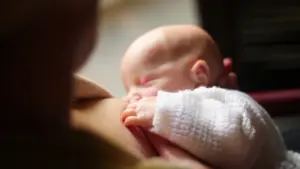 Moteris maitina savo miegantį kūdikį, užtikrindama jaukumą ir saugumą kelionės metu.