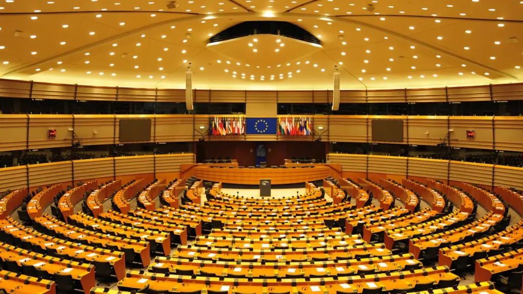 Tuščia Seimo ar parlamento posėdžių salė su mediniais stalais ir kėdėmis