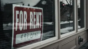 Raudonas skelbimas su užrašu „For rent“ ant gyvenamojo namo lango stiklo.