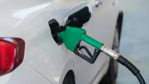 Degalų pylimo pistoletas įstatytas į balto automobilio kuro baką degalinėje.