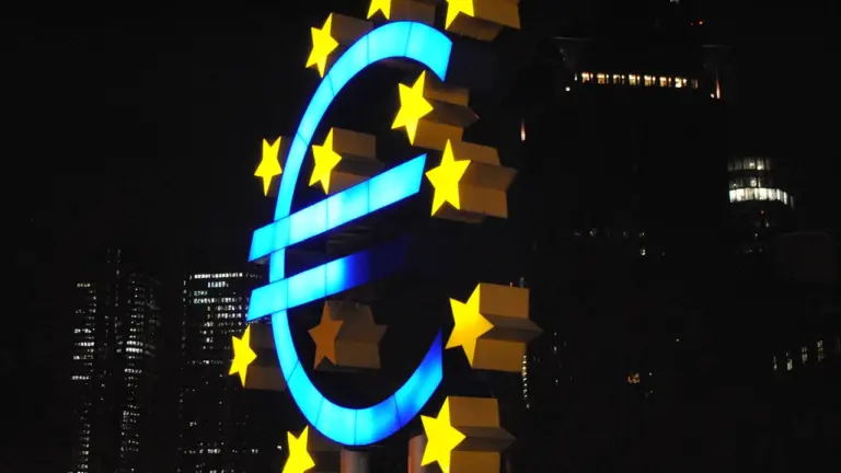 Didelis šviečiantis euro simbolis naktiniame mieste prie Europos centrinio banko pastato.