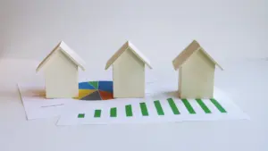 Mediniai nameliai ant popieriaus lapo su augančiu finansiniu grafiku ir diagramomis.