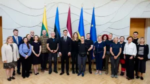 Grupė oficialiai apsirengusių žmonių stovi prie Lietuvos, Estijos, Latvijos, Ukrainos ir Europos Sąjungos vėliavų.