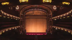 Istorinė teatro salė su apšviesta scena ir uždaryta uždanga Kauno naujienų portalui.