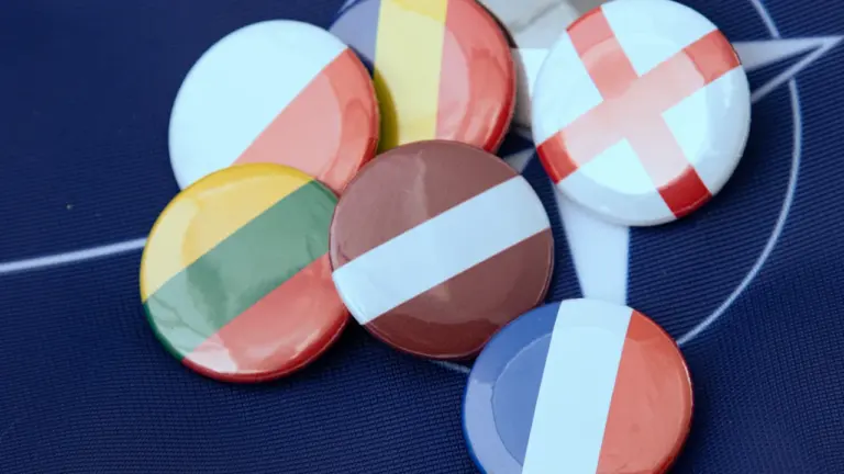 Kolekcija spalvotų ženklelių su Europos valstybių vėliavų motyvais ant tamsaus pagrindo.