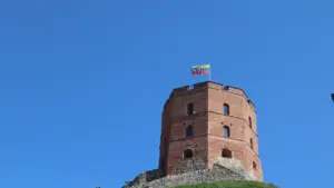 Gedimino pilies bokštas su plevėsuojančia Lietuvos vėliava žaliame kalne po giedru dangumi