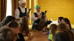 Dvi moterys tautiniais drabužiais rodo vaikams, kaip rišti tradicines verbos iš džiovintų žolelių.
