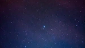 Tamsus naktinis dangus su gausybe ryškių žvaigždžių tamsiai mėlyname fone.
