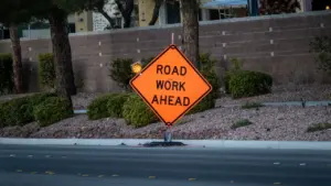 Oranžinis įspėjamasis kelio ženklas „Road Work Ahead“ pastatytas miesto gatvės pakraštyje.