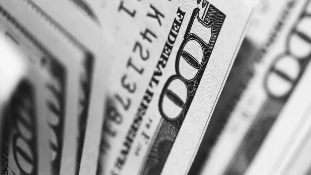Iš arti nufotografuoti šimto dolerių banknotai, simbolizuojantys sapnų temas apie finansus ir vertę.