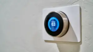 Išmanusis termostatas rodo namų temperatūrą ant baltos sienos šildymo sezono metu.