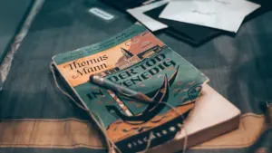 Senovinė knyga su pieštuku ant medinio stalo, skirta literatūros renginio pristatymui.
