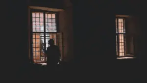 Siluetas tamsiame kambaryje žvelgia pro didelį langą laukdamas atsakymų ir aiškumo