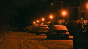Snieguota Vilniaus gatvė naktį su stovinčiais automobiliais ir apšviestais šaligatviais.