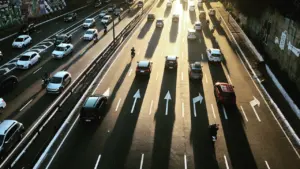 Saulėtas ryto eismas greitkelyje su ilgais automobilių šešėliais ir ženklinimu