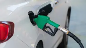 Degalų pistoletas įstatytas į balto automobilio kuro baką degalinėje pildymo metu